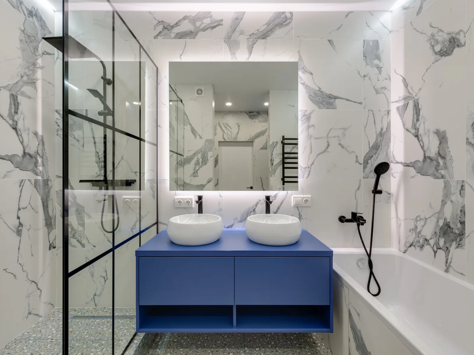 Marble bathroom with blue double vanity and backlit mirror
